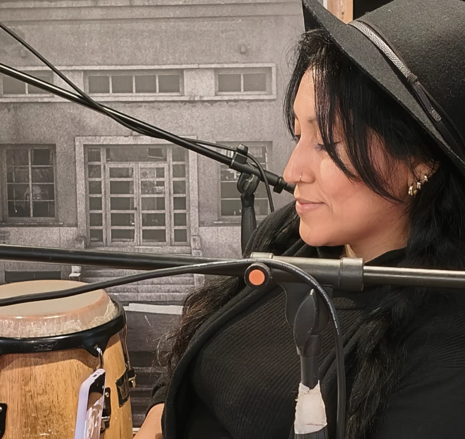 Francisca Huaman Quispe canta al microfono, cappello nero e congas accanto