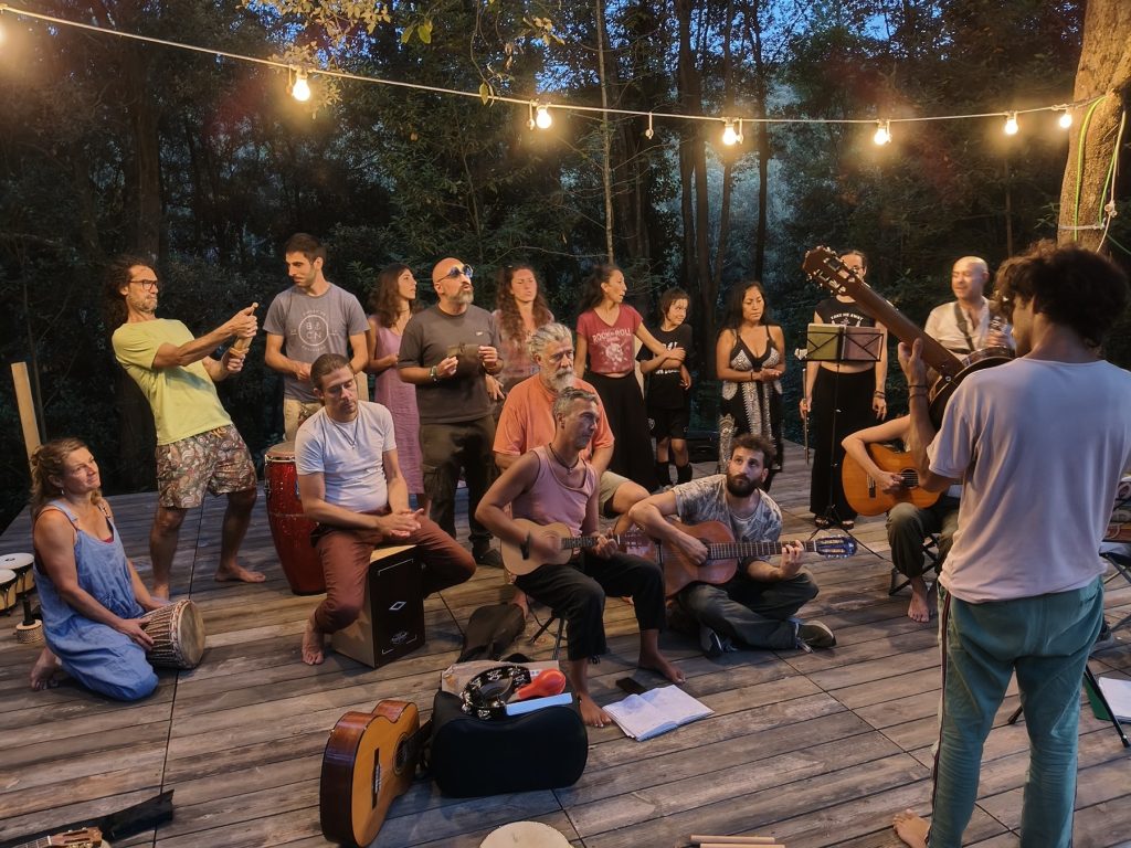 Un gruppo numeroso del Colectivo prova insieme sulla pedana nel bosco, con voci, chitarre e percussioni