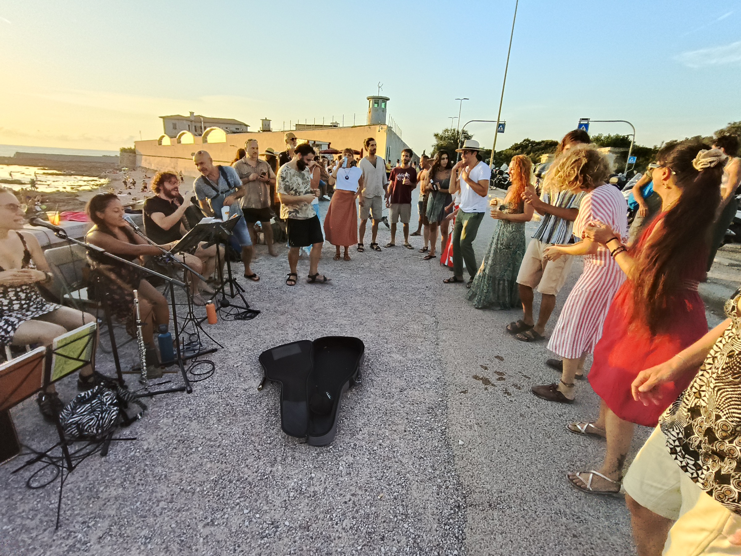 Il Colectivo al tramonto sul lungomare: a sinistra chi suona chitarre e percussioni, a destra una fila di persone che balla